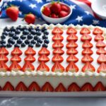 Homemade American flag cake decorated with blueberries and sliced strawberries on white frosting